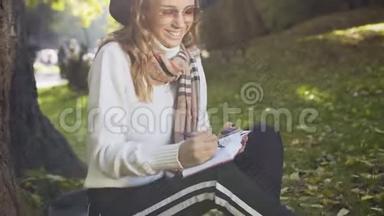 在城市<strong>公园里坐在</strong>草地上的年轻女子近距离拍摄，并在笔记簿上写了一些信息。